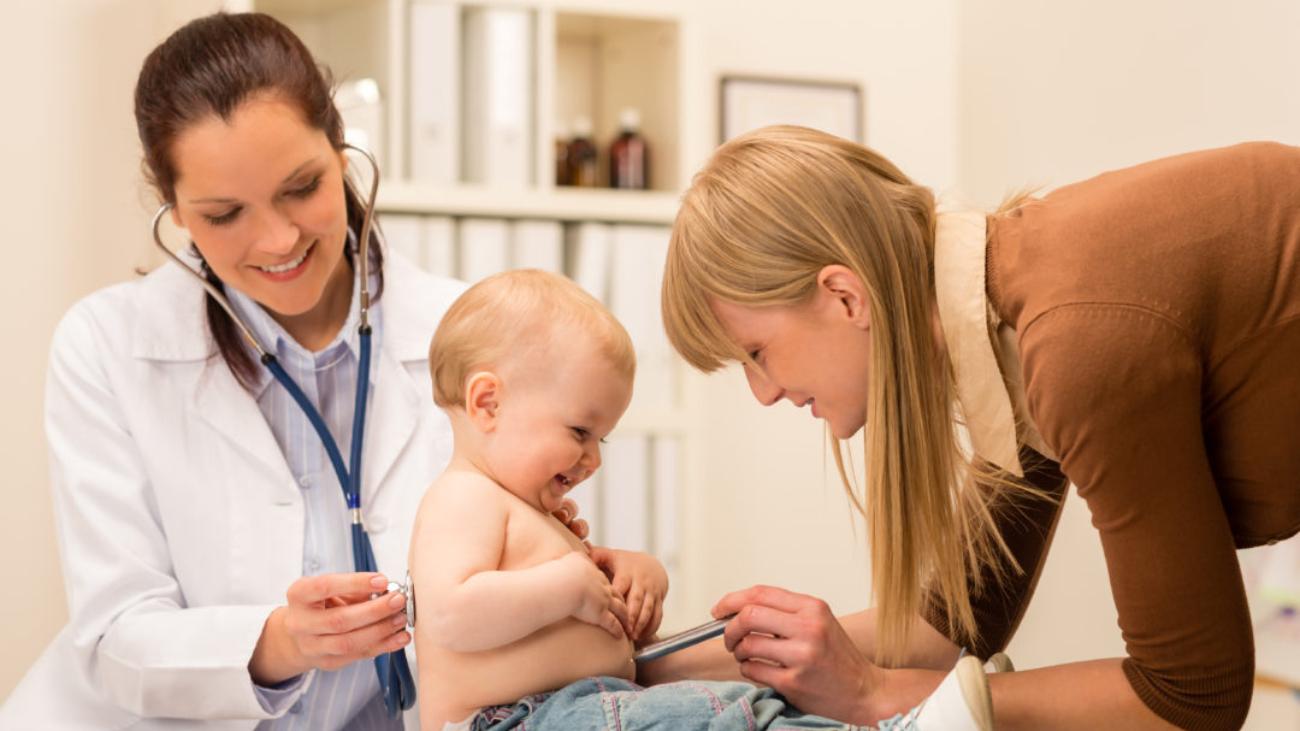 Female pediatrician checking cute baby girl with stethoscope mother assistance